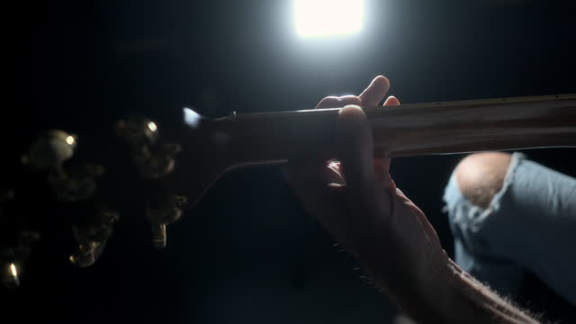 Rear view of man playing guitar with strong background lighting. Quarter stop pro mist filter. 60fps.
