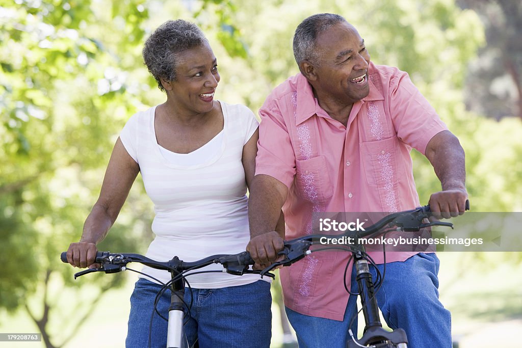 Older couple riding bikes in park Senior couple on cycle ride in countryside looking into distance smiling Senior Adult Stock Photo