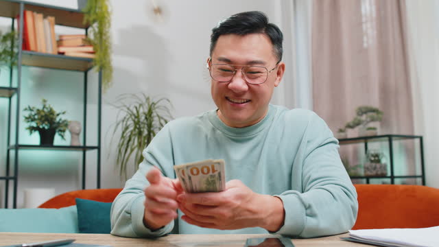 Rich happy Asian man counting money cash on smartphone calculator app, calculate income earnings