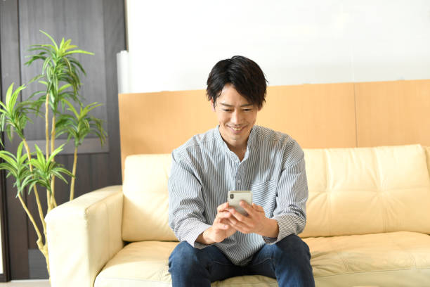 istock Smiling young Asian man sitting on the sofa while holding a mobile phone 1792100068