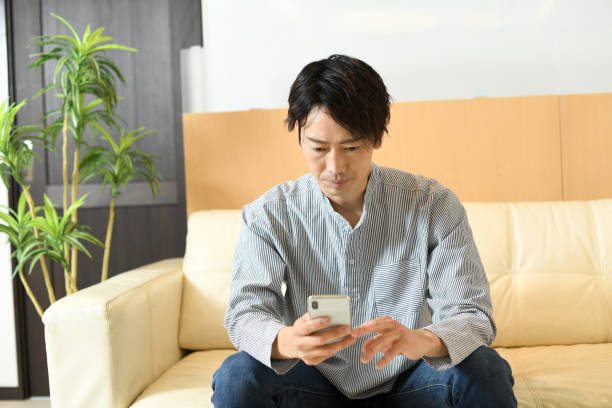 istock Smiling young Asian man sitting on the sofa while holding a mobile phone 1792101679