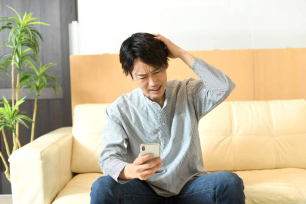 istock A young Asian man is worried while holding his mobile phone while sitting on the sofa. 1792103850
