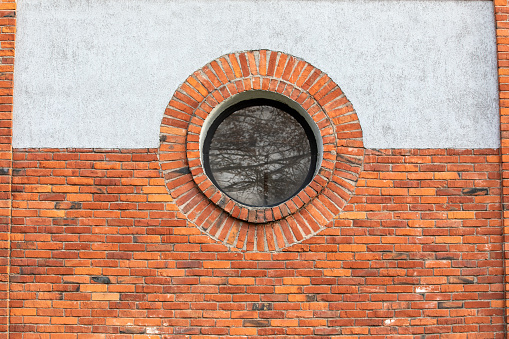 Round window. Red brick wall and light plaster.