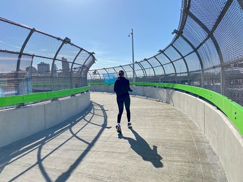 New York, NY USA - February 15, 2023 : Female jogger running up a curved ramp on the north walkway of the George Washington Bridge on a sunny winter day in Washington Heights, New York City