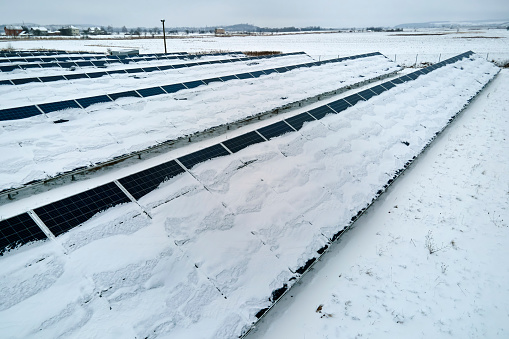 Aerial view of sustainable electrical power plant with solar photovoltaic panels covered with snow in winter for producing clean energy. Concept of low effectivity of renewable electricity in north.