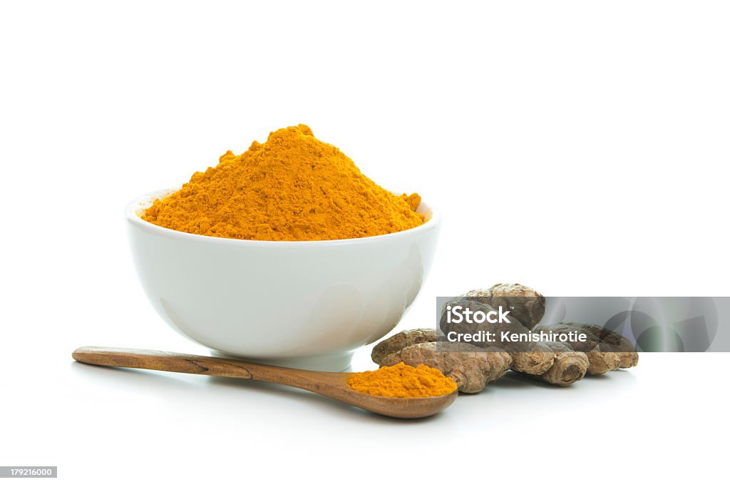 Tumeric powder in a white bowl with wooden spoon Bowl of turmeric powder with fresh turmeric root Turmeric Stock Photo