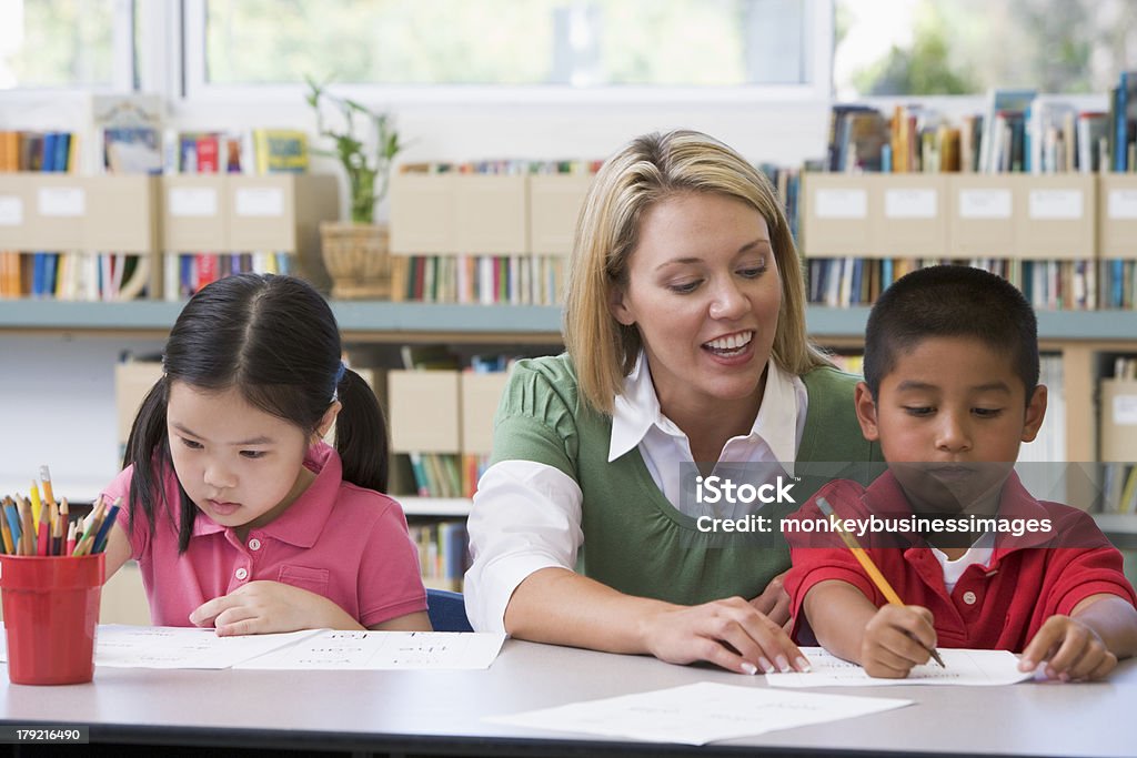 Kindergarten teacher helping students with writing skills Kindergarten teacher helping students with writing skills in classroom looking at pupils work 30-39 Years Stock Photo