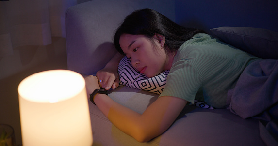 Portrait of Young Asian woman lying and looking at a health tracker in bed at night. Bedtime and rest concepts.