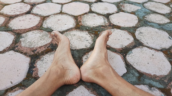 Close-up photo of a pair of feet with heels touching against a hexagonal paving background. Selective focus. Lifestyle concept