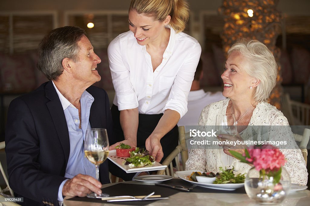 Waitress Serving Food To Senior Couple In Restaurant Waitress Serving Food To Senior Couple In Restaurant Looking At Each Other Smiling Restaurant Stock Photo