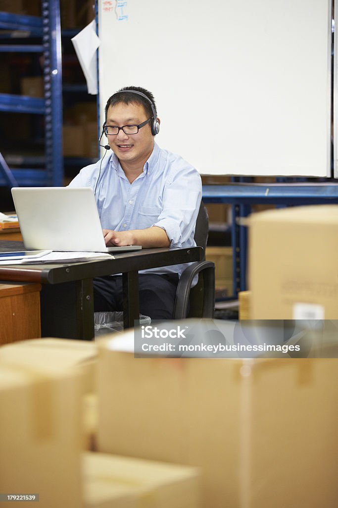 Trabalhador em armazém usando fone de ouvido e usando o Laptop - Foto de stock de 20 Anos royalty-free