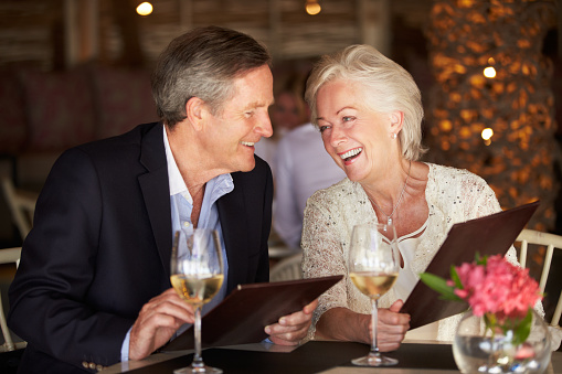 Senior Couple Choosing From Menu In Restaurant Chatting To Each Other Smiling