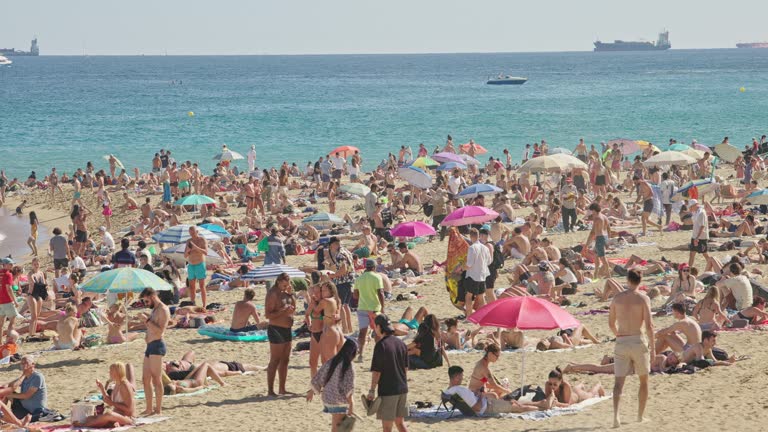 Crowd people sunbathing under a bright sun at Barceloneta beach on summer weekends.