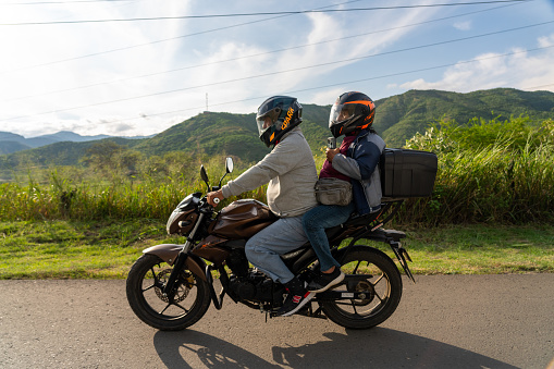 Two people riding a motorcycle on a country road at sunset time. Valle del Cauca . Colombia. October 9, 2023.
