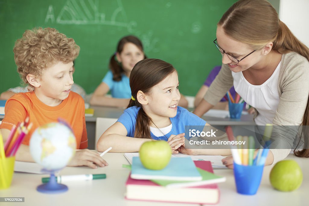 Talking to teacher Portrait of diligent schoolkids and teacher interacting at lesson Adult Stock Photo