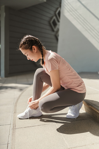 Young Asian woman tying shoelace on her running shoes. Preparation before jogging exercise. Fitness and sport activity. Healthy exercise concept.