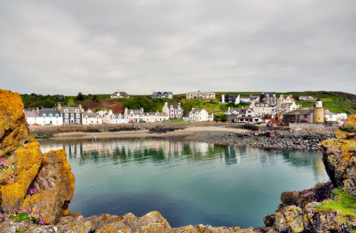 Tranquil view of Portpatrick harbour in southwest Scotland,lined with pretty houses and framed by lichen covered rocks in the foreground