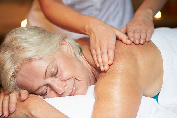 femme âgée ayant de massage dans le spa - health spa spa treatment towel candle photos et images de collection
