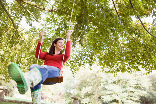 Young woman on garden swing looking into distance smiling