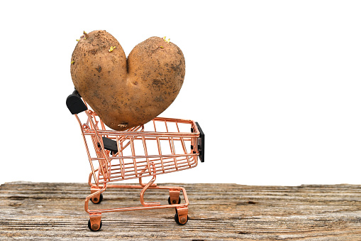 Heart shaped potato against a shopping cart on weathered wooden table over a white