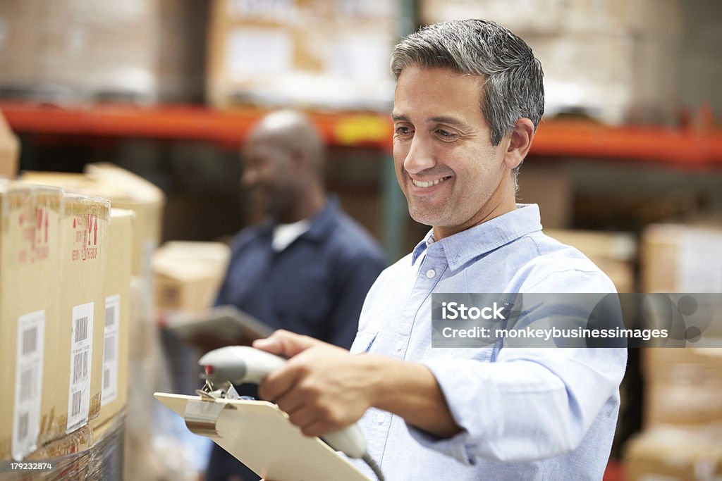 Man holding a clipboard and scanning packages in a warehouse Male Worker Scanning Package In Warehouse Bar Code Reader Stock Photo