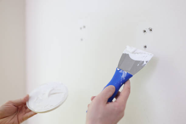 Hands with a spatula and putty near the wall, close-up Hands with a spatula and putty against the background of a white wall, a close-up. Scatter holes on the wall hand with a plaster spatula stock pictures, royalty-free photos & images