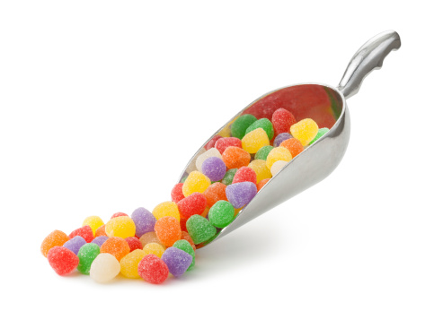 Assorted Gumdrops being served in a Metal Scoop.  Gumdrops are a type of candy. They are usually brightly colored gelatin and are shaped like a cone.  They come in different, artificial fruit flavors.  They are coated in granulated sugar.  This candy is a favorite around Christmas time. The image is shown at an angle, and is in full focus from front to back.  The image is isolated on a white background.