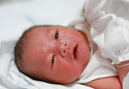 Close-up face of newborn Asian baby in the blanket. Open eyes.