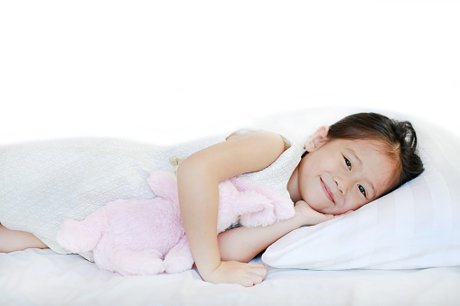 Portrait of a sweet smiling little Asian girl lying on bed in the morning with looking at camera.