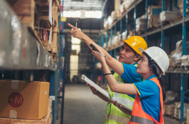istock Warehouse management team check stock inventory. Asian men women worker use bar code scaner scan goods shelf writing checklist on clipboard. Teamwork logistics staff counting products store inventory 1792333747