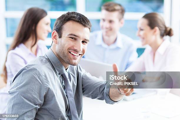 Smiling Man Giving Thumbs Up With Colleagues Blurred Stock Photo - Download Image Now