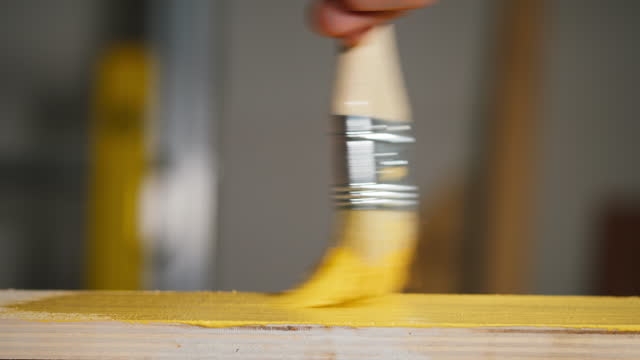 Painting wood with yellow paint using brush close-up. Renovation concept. Watercolor or acrylic texture. Home interior improvement, overhaul.