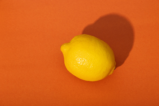 A whole lemon on an orange backdrop with hard light.