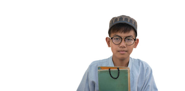 Boy sitting in mosque reading Quran. The child is sitting on the carpet under the light shining from the window of the mosque. He is reading the Quran in the lectern. worshiping. Shot with a full frame camera.
