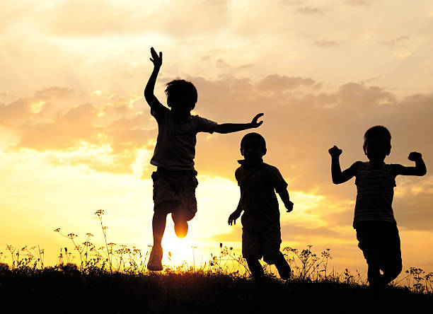 enfants courir sur prairie au coucher du soleil - three boys photos et images de collection