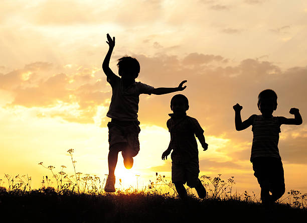 Children running on meadow at sunset stock photo