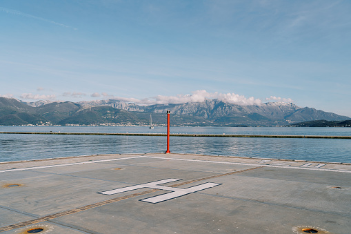 Helipad on the pier with a signal beacon by the sea against the backdrop of the mountains