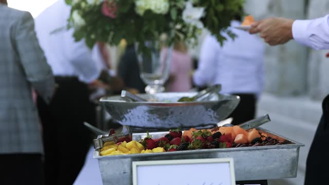 Guest puts exotic fruit slice on plate from elegant wedding reception buffet