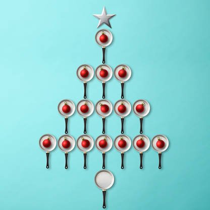 Close-up of Christmas tree made from a frying pans with red Christmas ornaments, on light blue background.