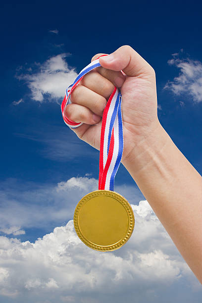 istock Golden medal in man's hand isolated with blue sky. 179245679