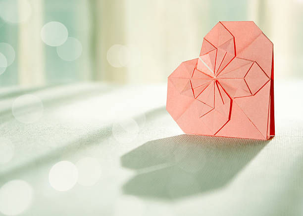 Sunlit pink origami paper heart with shadow in front stock photo