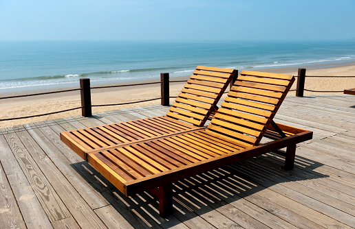 Two wooden beach chairs on a deck overlooking the ocean