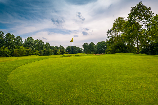 golf course with yellow flag on 18th hole at cloudy sky