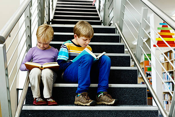 istock Happy bookworm brother and sister reading on library steps 179249332