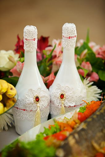Bottle on the table for the wedding, decorated with lace and flowers.