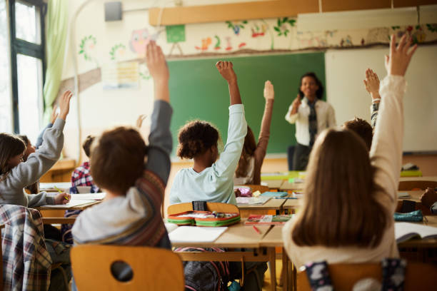 istock Back view of students raising their hands to answer the teacher's question on a class. 1792525618
