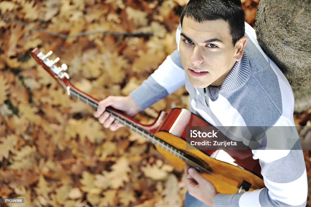 Giovane uomo con chitarra nel parco - Foto stock royalty-free di Abiti pesanti