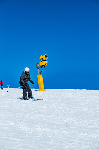 Skier equipped with ski-wear going slowly down the slope covered in beautiful white snow in the mountains on a clear winter day