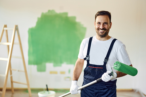 Portrait of happy male worker painting the wall in green color and looking at camera. Copy space.