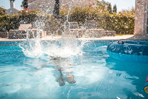 A joyful young boy of mixed race, having fun as he jumps into the pool at a villa.